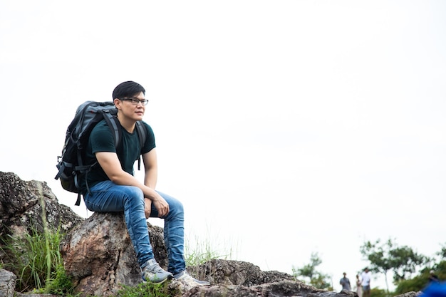 白い背景の上の夏の岩山の崖の上に座ってリラックスした旅行者の男。旅行ライフスタイルハイキングコンセプト夏休み屋外