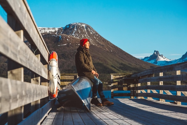 Un viaggiatore si siede in una barca vicino a un molo di legno sullo sfondo di un lago di montagna per il testo o