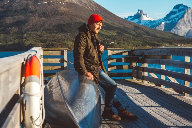 Путешественник сидит в лодке возле деревянного пирса на фоне горного озера место для текста или