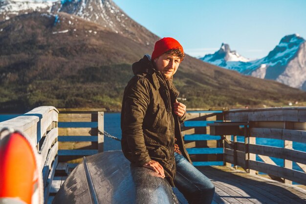 Traveler man sits in a boat near a wooden pier on a background of a mountain lake place for text or