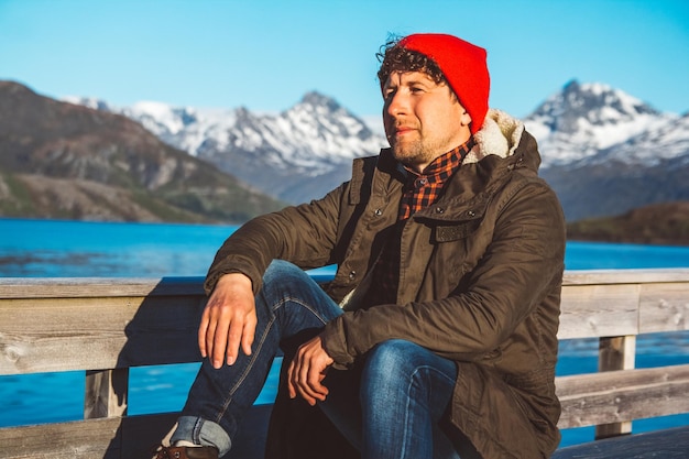 Photo traveler man sits in a boat near a wooden pier on a background of a mountain lake place for text or