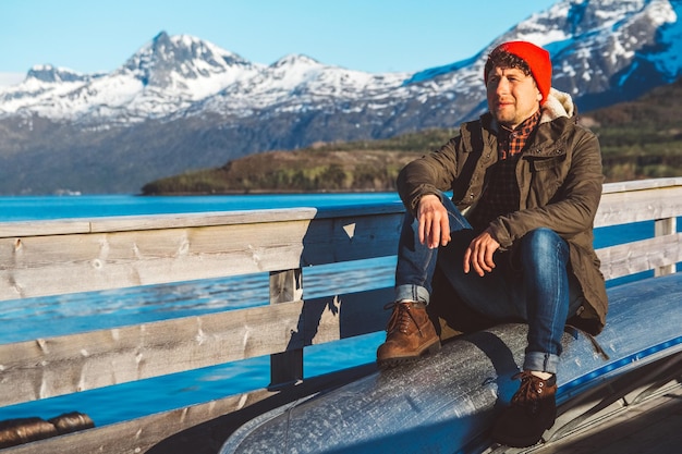 Traveler man sits in a boat near a wooden pier on a background of a mountain lake