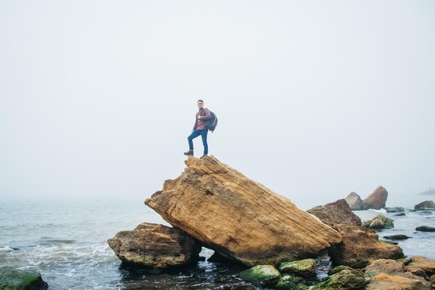 Человек-путешественник стоит на скале на фоне красивого моря. Место для текста или рекламы