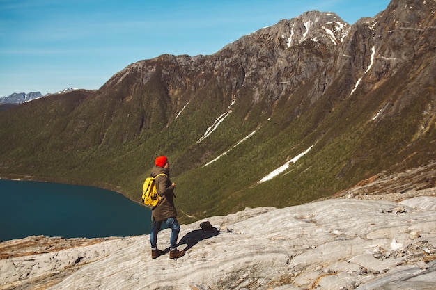 Traveler man with a backpack standing on a rock on the background of a glacier mountains and snow