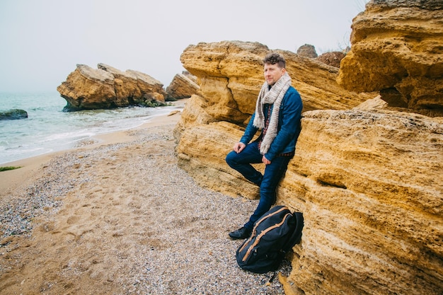 바다를 배경으로 바위 한가운데 있는 모래사장에 배낭을 메고 서 있는 여행자