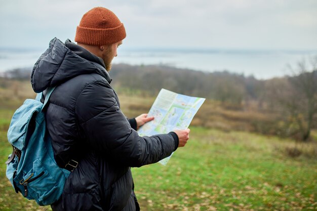 Uomo viaggiatore con zaino con mappa in mano su uno sfondo di montagne fiume della natura, concetto di viaggio, vacanze e concetto di escursionismo lifestyle