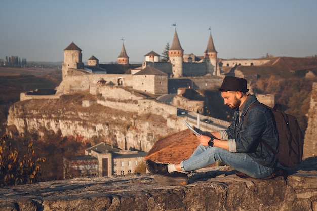 Traveler man with a map in his hands sits on the background of the old castle