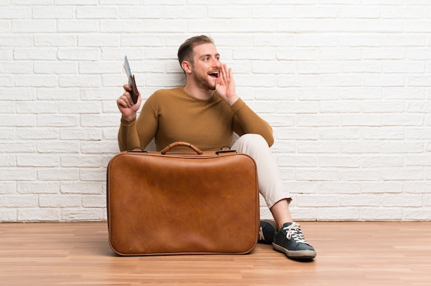 Traveler man with suitcase and boarding pass shouting with mouth wide open