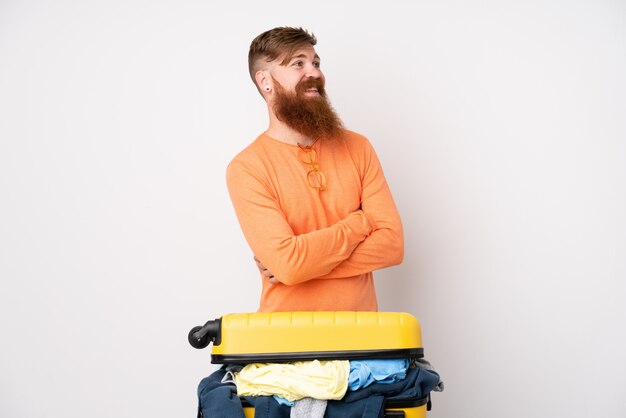 Traveler man with a suitcase full of clothes over isolated white laughing