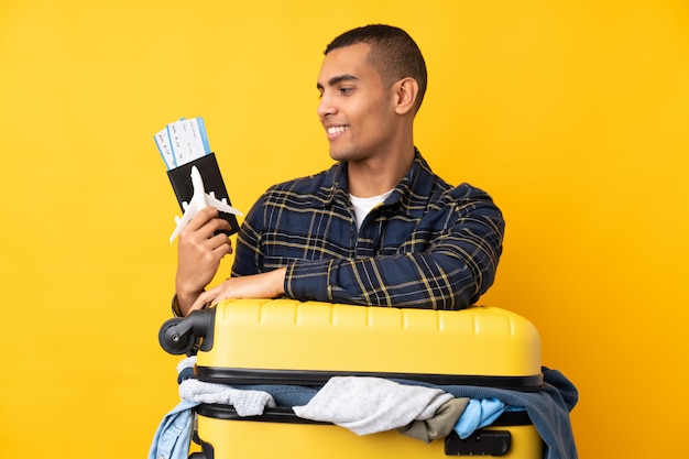 Traveler man with a suitcase full of clothes over isolated yellow wall