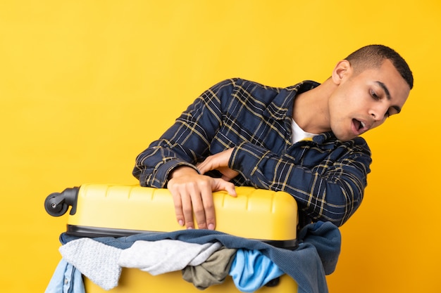 Traveler man with a suitcase full of clothes over isolated yellow wall