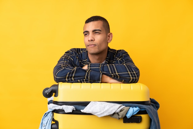 Traveler man with a suitcase full of clothes over isolated yellow wall