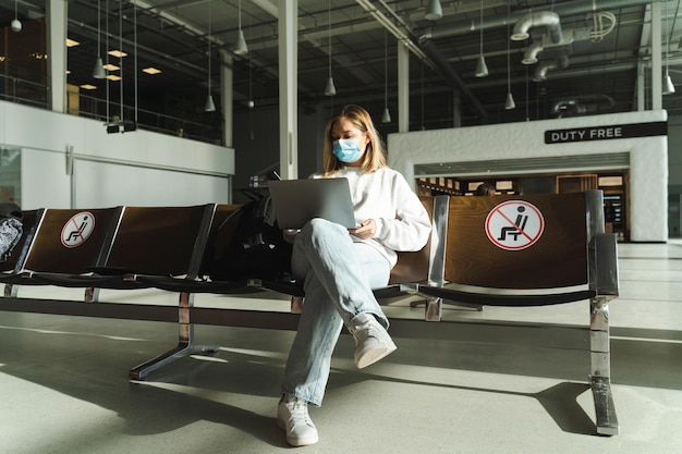 Traveler in mask sitting in airport lobby chair with social distancing sign