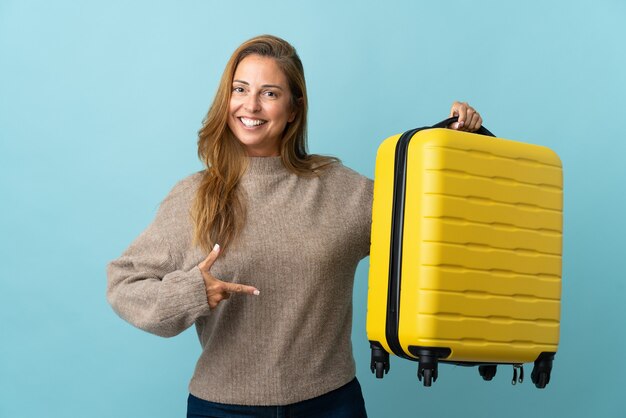 Traveler middle age woman holding a suitcase isolated on blue wall in vacation with travel suitcase