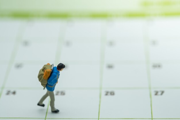 Traveler miniature figure people with backpack walking on calendar