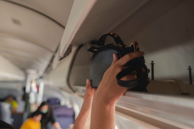 Photo traveler open overhead locker on airplane handluggage compartment with suitcases in airplane