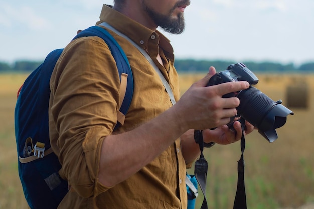 Fotografo viaggiatore con una macchina fotografica in mano sullo sfondo di un campo e mucchi di fieno