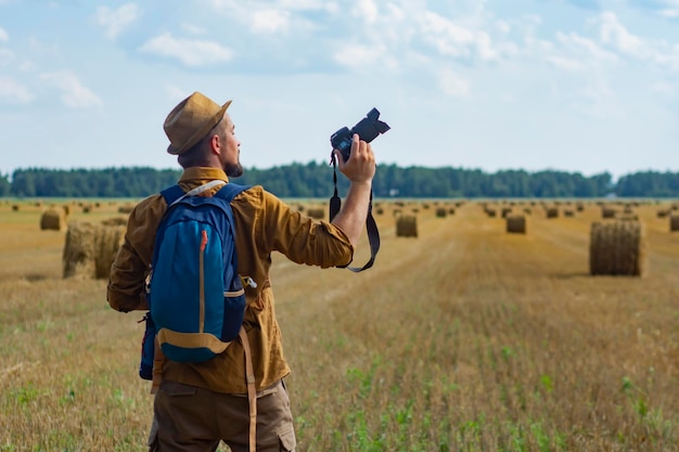 Fotografo viaggiatore con una macchina fotografica in mano sullo sfondo di un campo e mucchi di fieno