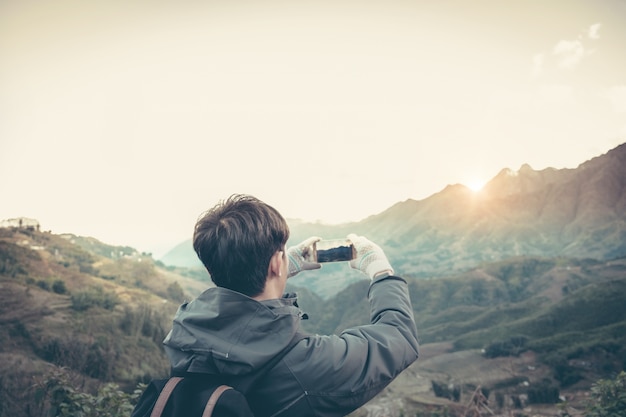 スマートフォンで山と太陽と空を撮影する旅行者。