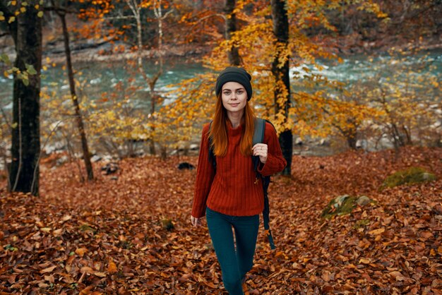 Путешественник в красном свитере и шляпе гуляет по осеннему лесу у горной реки, вид сверху