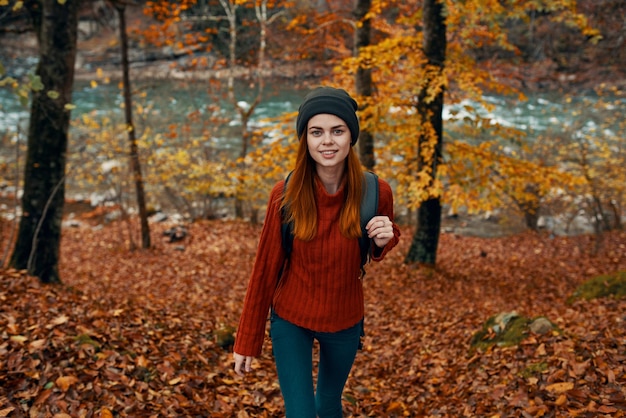 빨간 스웨터와 모자를 쓴 여행자가 산 강 평면도 근처의 가을 숲에서 산책