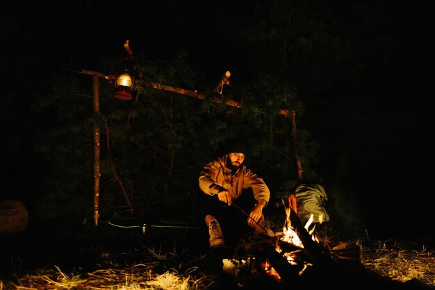 The traveler rests by the night campfire Furnished shelter from branches for sleeping with a kerosene lamp and a fire surrounded by stones