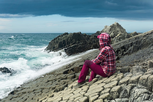 Traveler sits on the shore of a stormy sea on a natural pavement made of columnar granite