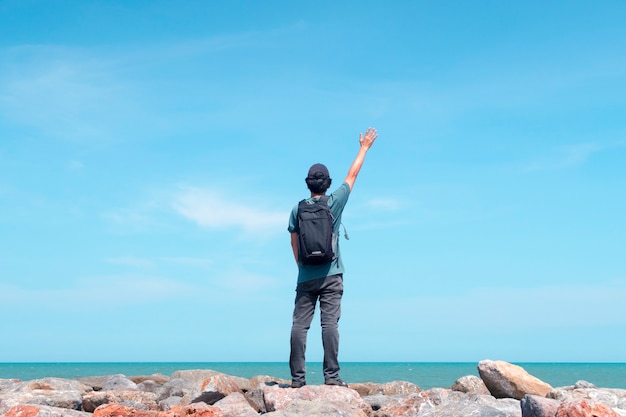 Traveler standing and raising his hand on a rock looking at the sea
