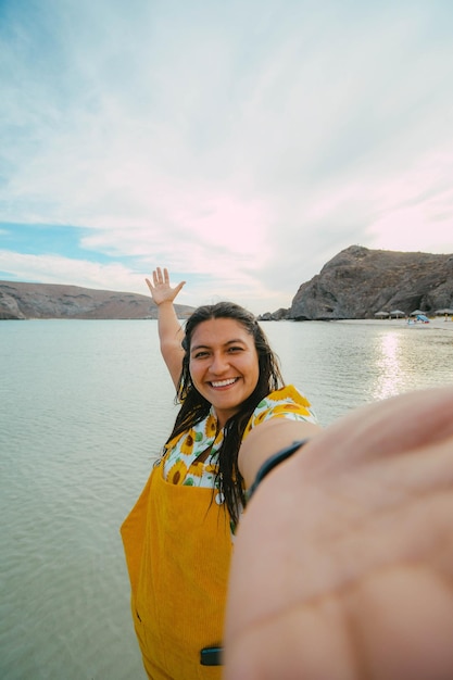 彼女がいる場所を示すソーシャルネットワークのために自分撮りをしている旅行者バランドラビーチバハカリフォルニアスル