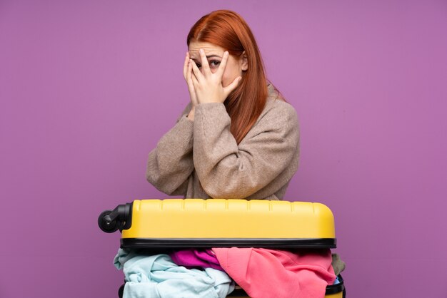 Foto ragazza dell'adolescente del viaggiatore con una valigia piena di vestiti che coprono gli occhi e che guardano attraverso le dita