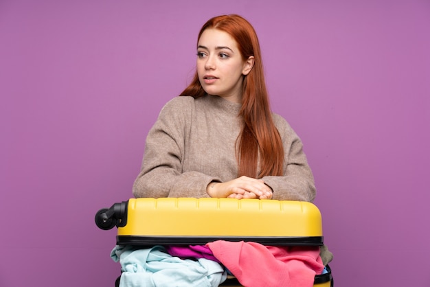 Traveler teenager girl with a suitcase full of clothes looking side