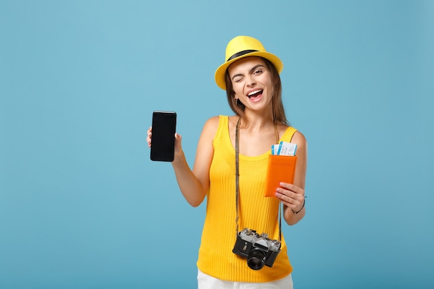Donna turistica del viaggiatore in cappello giallo dell'abbigliamento casual che tiene la macchina fotografica del cellulare dei biglietti su blue