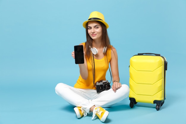 Traveler tourist woman in yellow casual clothes, hat with suitcase mobile phone on blue