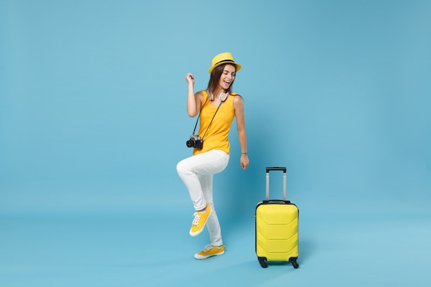 黄色のカジュアルな服を着た旅行者の観光客の女性、青いスーツケースの写真カメラと帽子