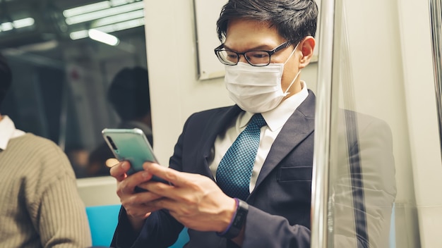 公共電車で携帯電話を使用しながらフェイスマスクを着用している旅行者