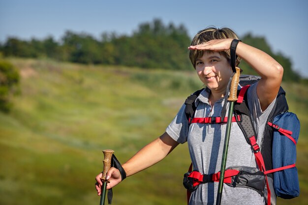 Traveler with a backpack and hiking sticks. Woman traveler looking to protect your eyes from the sun by hand. Photographed in Russia.