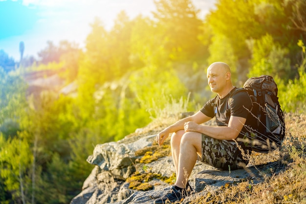 A traveler with a backpack on his shoulders sits on a rock 