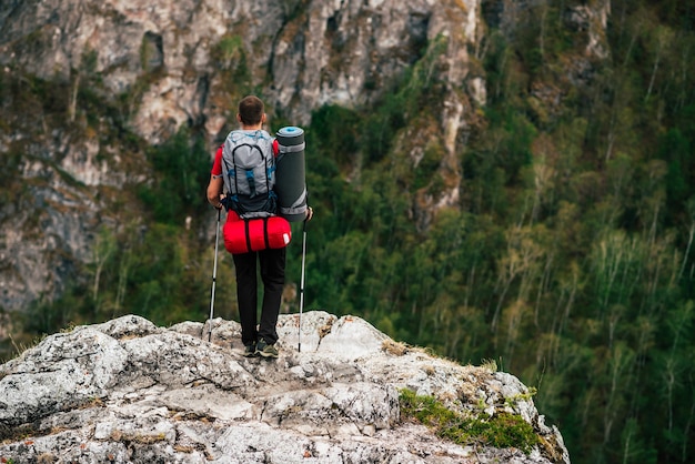 A traveler with a backpack in the mountains, rear view. The concept of a sporty lifestyle in travel. A man with a backpack in the mountains. Hiking in the mountains. Outdoor activities. Copy space