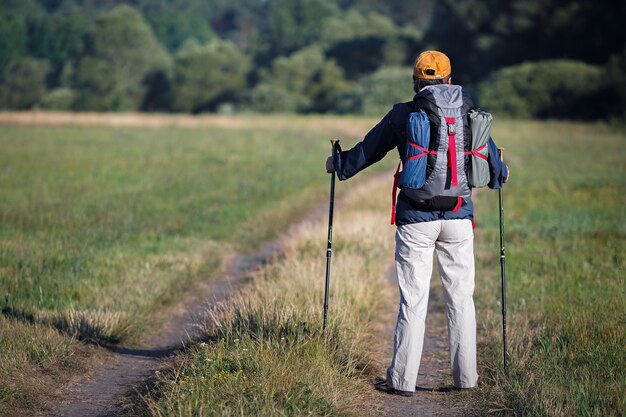 バックパックとトレッキングスティックを持った旅行者。早朝に牧草地に立っている観光客。後ろからの眺め。ロシアで撮影。