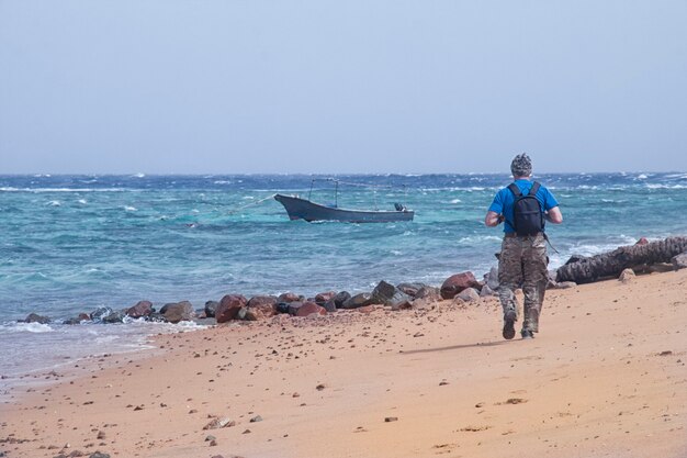 The traveler with a backpack walks along the sandy shore during a storm at sea in solitude