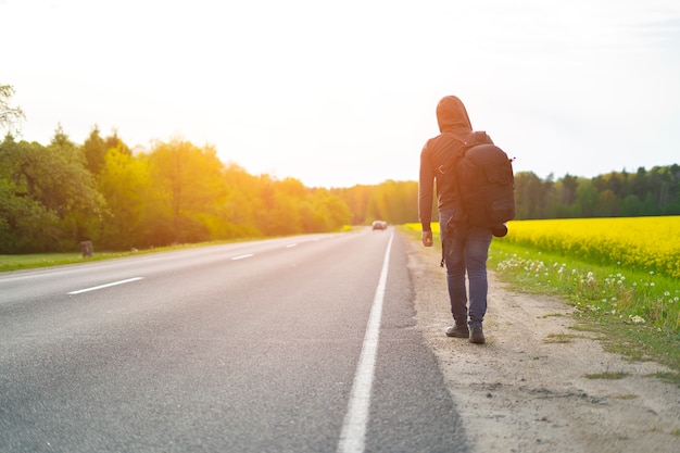 大きなバックパックを背負った旅行者が道路脇の道を歩いている