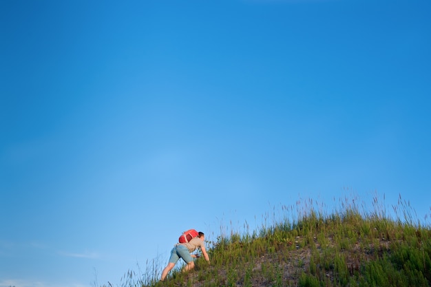 青い空を背景に丘でハイキングオレンジバックパックを持つ旅行者
