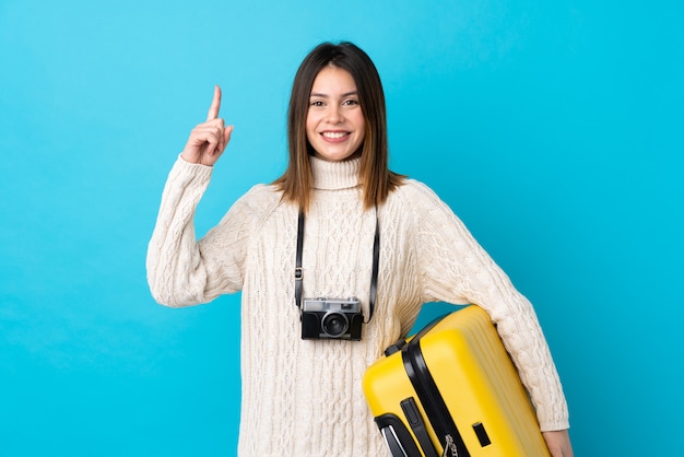 Traveler woman holding a yellow suitcase over isolated blue wall