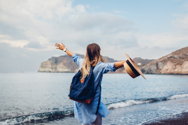 Traveler woman running along shore of Red beach on Santorini island, Greece. Traveling and vacation concept