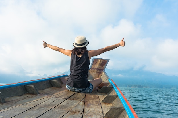 Traveler woman sit at the head of traveling wooden boat and raised hands up on the sea or 