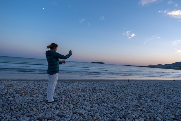 Traveler woman taking photo on rocky beach at sunset