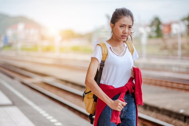 Женщина-путешественник идет и ждет поезда на железнодорожной платформе