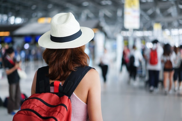 La donna del viaggiatore che porta il cappello e porta la borsa che sta dentro l'aeroporto dopo il volo di registrazione