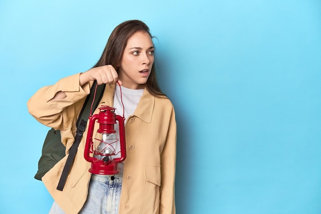 Traveler woman with backpack holding a lantern on blue background