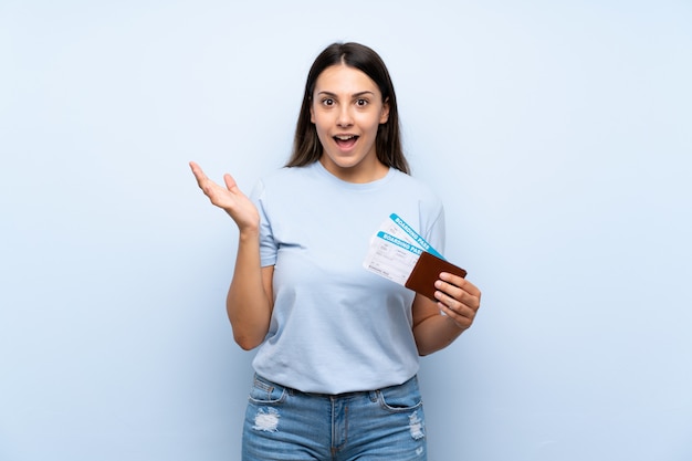 Traveler woman with boarding pass over isolated blue wall with shocked facial expression